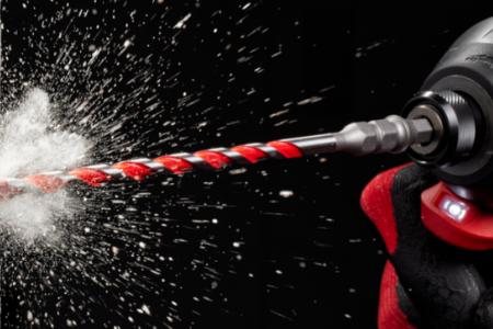 Power drill with red bit drilling into a black background