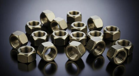 Collection of brass hex nuts on a reflective surface with a dark background